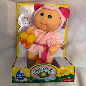 May include: A Cabbage Patch Kids Tiny Newborn doll in a pink robe with a matching hood and a rubber duck. The doll is in a box that says "Bubble 'n Bath" and "I can float in the tub!"