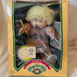 NOS 1985 Coleco Cabbage Patch Kid – Zeldzame outfit met violette ogen, lange blonde lokken en ultra-zeldzame jurk met drie hartjes (in originele verpakking)