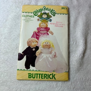 May include: A Butterick sewing pattern envelope, number 3927, for Cabbage Patch Kids clothes. The front features illustrations of dolls in a pink dress, a black tuxedo, and a white wedding gown with a veil. Text includes Cabbage Patch Kids, CLOTHES, and SORRY NO RETURNS ON PATTERNS FABRICLAND.