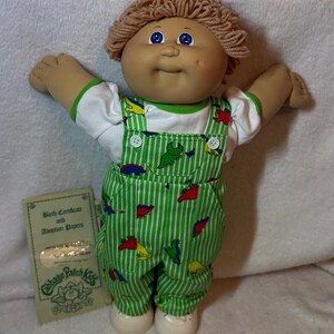 Muñeco Cabbage Patch Kid vintage – Cabello rizado color champán, ojos azules, un solo hoyuelo con overol de dinosaurio réplica personalizado y papeles de adopción.