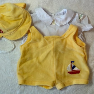May include: A yellow baby outfit set, including a sun hat, a romper with a sailboat design, and a white collared shirt. The hat has a red anchor emblem. The romper has a red, white, and blue sailboat applique.