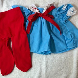 May include: A baby doll outfit featuring a light blue dress with a red bow and white lace trim. The outfit includes a pair of bright red tights. The dress has short sleeves and a gathered skirt.