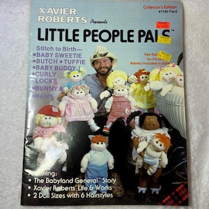 May include: A softcover book titled Xavier Roberts Presents Little People Pals featuring a photograph of a man wearing a cowboy hat surrounded by several fabric dolls with yarn hair and various outfits. The cover includes text listing doll names.