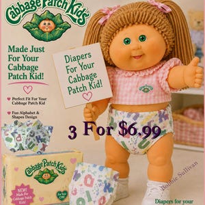 May include: A Cabbage Patch Kids doll wearing a pink gingham top and patterned diaper holds a sign that reads "Diapers For Your Cabbage Patch Kid!". The image includes a box of diapers and a diaper with alphabet and shape designs.