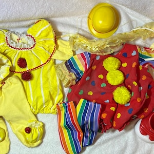 May include: A collection of clown costumes in yellow and red. The outfits include a yellow hat, pants, and top with red accents, and a red outfit with yellow pom-poms. Also included are red and white shoes and a yellow hat.