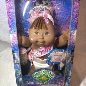 May include: A Cabbage Patch Kids Millennium Celebration doll in its original packaging. The doll has brown skin, brown hair, and is wearing a white diaper and a sash that says "2000". The packaging includes the text "Collector Edition".