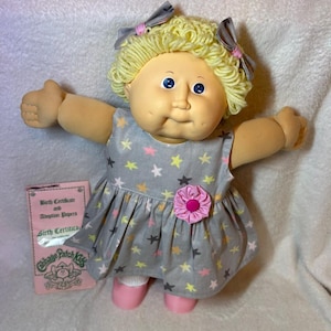 Muñeca Cabbage Patch Kid vintage de los años 80 - Coleco CPK, cabello rubio de lana, ojos azules, con certificado de nacimiento original y vestido de estrella personalizado.