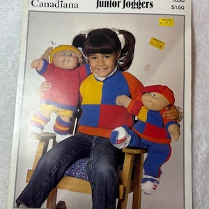 May include: A vintage knitting pattern booklet titled Patons Canadiana Junior Joggers, featuring a color photograph of a child wearing a color-blocked sweater in red, yellow, and blue, holding two dolls dressed in matching knitted outfits and hats.