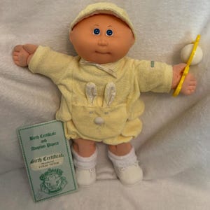 May include: A white ceramic mug with a black handle and the text "But First, Coffee" in a bold, black font. The mug is set against a blurred background, suggesting a cozy setting.