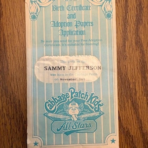 May include: A vintage Cabbage Patch Kids All Stars birth certificate and adoption papers application. The certificate is light blue with vertical stripes and features the name "SAMMY JEFFERSON" and the date "November 1st". The Cabbage Patch Kids logo is prominently displayed.