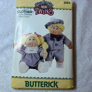 May include: A Butterick sewing pattern envelope for Cabbage Patch Kids Twins, number 3564. The package features an illustration of two dolls with blonde yarn hair wearing matching lavender outfits, including a dress with a white collar and a suit.