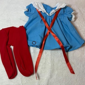 May include: A baby blue dress with a white lace collar and red ribbon straps. The dress has short sleeves with lace trim. A pair of red tights is next to the dress. The outfit is likely for a baby or toddler.