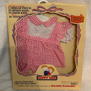May include: A vintage Happy Kids doll clothes set for 16" dolls. The set includes a pink gingham dress with white collar and sleeves, and a matching pair of shorts. The packaging features the Happy Kids logo and text that reads "Dress Your Kids Like The Real Kids!"