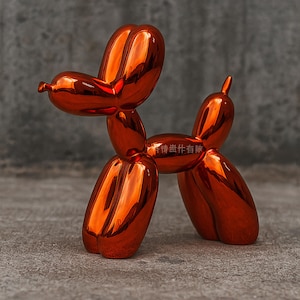 Op de afbeelding: Een glanzende, oranje-rode ballonhondsculptuur. De hond is gemaakt van een reflecterend materiaal, met een glad, gebogen oppervlak. De sculptuur is een speels, modern kunstwerk, ideaal voor interieurdecoratie.