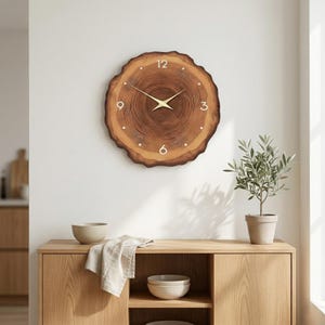 Puede incluir: Un reloj de madera redondo con diseño de rodaja de árbol. La esfera del reloj tiene números blancos y manecillas doradas. El reloj está montado en una pared blanca sobre un mueble de madera. Diámetro: aprox. 30 cm.