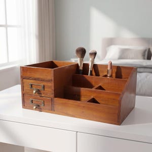 May include: A wooden makeup organizer with two small drawers and multiple compartments. The organizer holds makeup brushes and a lipstick. The wood has a warm, brown tone, and the drawers have brass-colored pulls.