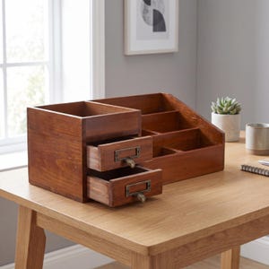 May include: A wooden desk organizer with a warm brown finish. It features two small drawers with metal handles and multiple compartments for storage. The organizer is designed to hold office supplies and keep a desk tidy.