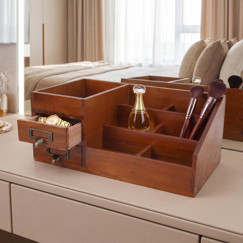 May include: A wooden vanity organizer with multiple compartments and a small drawer. The organizer is stained a warm brown color and holds a gold wristwatch, perfume bottle, and makeup brushes. The design is suitable for storing cosmetics and jewelry.