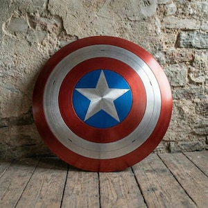 May include: A round shield with a red, silver, and blue color scheme. The shield features a silver star on a blue circle in the center, surrounded by concentric rings of silver and red. The shield is resting on a wooden surface.