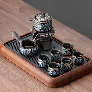 Puede incluir: Juego de té completo en marrón y negro. Incluye una tetera, una jarra y seis tazas pequeñas. Cada pieza está adornada con diseños florales azules. El juego se presenta sobre una bandeja de madera. Las tazas miden unos 5 cm de diámetro.