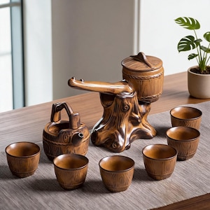 Puede incluir: Un juego de té de cerámica con textura de veta de madera marrón. El set incluye una tetera con forma de barril con asa, una tetera única inspirada en un tocón de árbol con pico largo y tapa, y seis tazas de té pequeñas a juego con acabado.