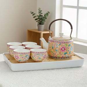 Könnte beinhalten: Ein Keramik-Teeservice bestehend aus einer Teekanne mit braunem geflochtenem Henkel und fünf passenden Teetassen. Das Set ist mit einem leuchtend orangefarbenen Hintergrund, komplexen Blumenmustern in Pink, Blau und Grün sowie Goldrändern verziert.