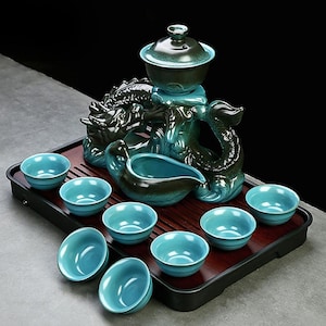 May include: A teal ceramic tea set featuring a dragon-shaped stand, a lidded teapot, a serving pitcher, and eight small teacups. The set is presented on a dark wooden tray, contrasting with the teal colour of the tea set.