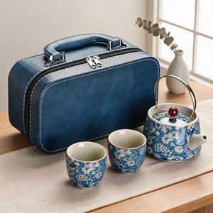 Könnte beinhalten: Ein blaues Teeservice mit einer Teekanne und zwei Tassen mit weiß-blauem Blumenmuster, dazu ein passender blauer Tragekoffer mit Tragegriff und Reißverschluss. Die Teekanne hat einen goldfarbenen Metallgriff und einen roten Perlenknauf.