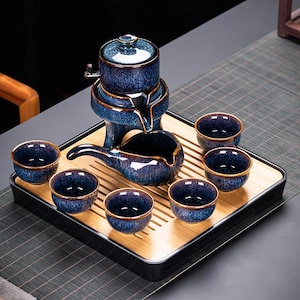 May include: A complete tea set with a blue and gold glaze. The set includes a tea maker, a serving pitcher, and six small tea cups. The tea set is displayed on a bamboo tray with a black border. The tea set is designed for tea ceremonies.