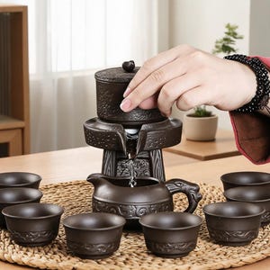 Puede incluir: Un juego de té de cerámica marrón oscuro que incluye una tetera con forma de piedra de molino con tapa y una jarra a juego con asa en forma de dragón, rodeado de ocho tazas pequeñas, todo decorado con intrincados patrones y texturas en relieve.