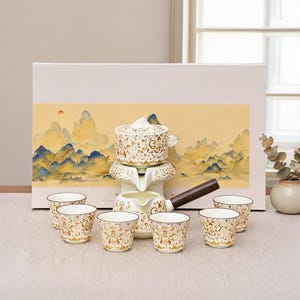 Pode incluir: Um conjunto de chá em cerâmica com um bule de cabo de madeira escura, um infusor empilhável e seis chávenas a condizer. Cada peça é decorada com um padrão floral intrincado em laranja, dourado e branco. O conjunto está em frente a uma caixa.