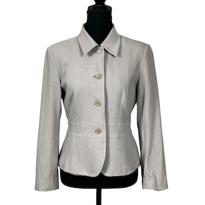 Pode incluir: Um blazer cinza-claro com gola estruturada, mangas compridas e fecho frontal com quatro botões circulares a condizer. A peça inclui um detalhe de costura horizontal na cintura, criando uma silhueta com a bainha ligeiramente alargada.