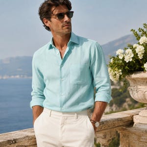 May include: A light turquoise long-sleeve button-down shirt with a single chest pocket, paired with white trousers. The shirt features a classic collar and light-colored buttons, worn with a wristwatch featuring a brown leather strap.