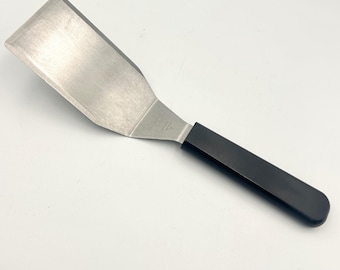 Espátula volteadora de acero inoxidable negro de alta resistencia de The Pampered Chef, fabricada en Taiwán.