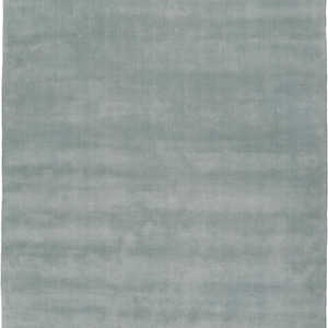 May include: A rectangular, light blue rug with a soft, textured appearance. The rug's color is a muted, pale blue, and the texture suggests a plush, comfortable feel. The design is simple, making it suitable for various interior styles.