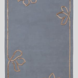 Pu&ograve; includere: Un tappeto rettangolare di colore blu ardesia a tinta unita caratterizzato da un bordo in rilievo color marrone chiaro che forma motivi floreali astratti e stilizzati in ognuno dei quattro angoli. Il design &egrave; coerente e simmetrico.
