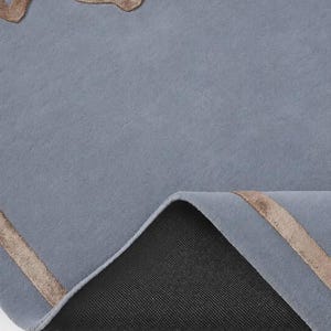 Pu&ograve; includere: Un tappeto blu con un motivo floreale in rilievo color bronzo metallizzato e bordi lineari. Il tappeto &egrave; parzialmente ripiegato per rivelare un materiale di supporto nero, testurizzato e antiscivolo sul lato inferiore della superficie.