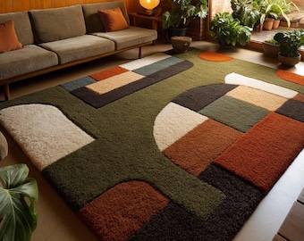 May include: A large, geometric area rug with a green background and abstract shapes in shades of brown, orange, beige, and white. The rug is placed in a living room setting with a sofa and plants.
