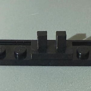May include: A black Lego baseplate with two raised rectangular studs and four round studs. The baseplate is a solid black color and appears to be made of plastic. The Lego baseplate is a building block for construction toys.