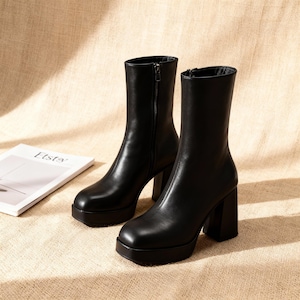 Pode incluir: Um par de botas pretas de plataforma com salto bloco. As botas têm bico arredondado e zíper na parte interna. São feitas de material liso e assentam sobre uma sola de plataforma.