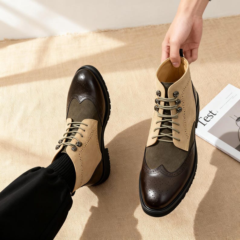 Op de afbeelding: Tweekleurige leren laarzen met een klassiek brogue-ontwerp. De laarzen hebben een combinatie van donkerbruine, olijfgroene en beige su&egrave;de panelen, met een vetersluiting en een stevige zwarte zool. Het woord "Test" is zichtbaar op een tijdschrift.