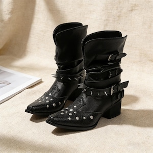 May include: A pair of black leather ankle boots with a pointed toe and a low block heel. The boots feature silver-toned metal studs and buckles, with a folded-over top. The boots are approximately 20 cm tall.
