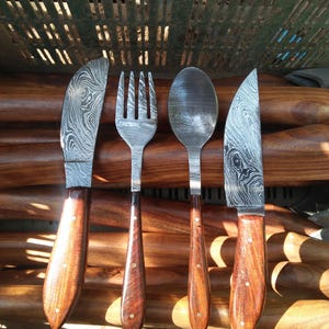 Può includere: Un set di quattro posate artigianali: un coltello, una forchetta e un cucchiaio, con un secondo coltello. Le lame hanno un design unico. Ogni utensile ha un manico in legno con rivetti in ottone.
