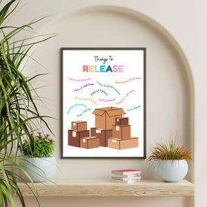 May include: A framed print with the words "Things to RELEASE" in colourful letters. The image features a stack of brown cardboard boxes with phrases like "Emotional baggage" and "Fear of rejection" written around them, suggesting a theme of letting go.