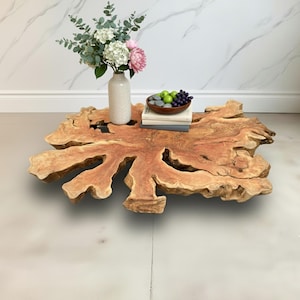 Puede incluir: Una mesa de centro de madera única, de forma libre, con borde natural. La mesa es de color marrón rojizo cálido y presenta un jarrón con flores, un cuenco de fruta y libros. Una pieza destacada para cualquier salón.