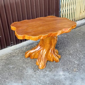 Op de afbeelding: Een handgemaakte houten tafel met een natuurlijke rand en een basis in de vorm van een boomstam. De tafel heeft een warme, roodbruine afwerking. De afmetingen zijn ongeveer 91 cm lang, 61 cm breed en 51 cm hoog.