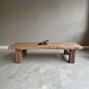 Puede incluir: Una mesa de centro rectangular de madera rústica con acabado natural. La mesa tiene cuatro patas robustas y dos cuencos pequeños encima. Las dimensiones de la mesa son de aproximadamente 152 cm de largo, 61 cm de ancho y 41 cm de alto.