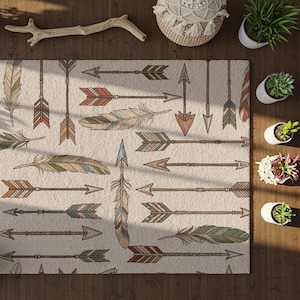 Op de afbeelding: Beige vloerkleed met een patroon van pijlen en veren in bruin, rood, groen en blauw. Het vloerkleed heeft een textuur en ligt op een houten vloer. Het ontwerp heeft een bohemien of zuidwestelijke stijl.
