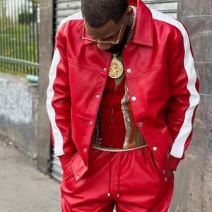 May include: A red leather jacket with white stripes down the sleeves and matching red pants. The jacket has a button-up front. A gold chain and pendant are visible.