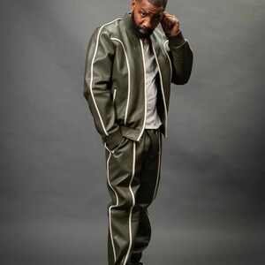 K&ouml;nnte beinhalten: Olivgr&uuml;ne Leder-Bomberjacke und passende Jogginghose mit wei&szlig;em Paspel. Die Jacke hat einen gerippten Kragen und B&uuml;ndchen. Die Hose hat einen elastischen Bund. Das Outfit wird mit wei&szlig;en Turnschuhen kombiniert. Ein stilvoller Streetwear-Look.